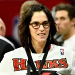Jami Gertz, najbogatija glumica, stoji ispred logotipa NBA tima Atlanta Hawks, simbolizirajući spoj njezine glumačke i poslovne karijere.